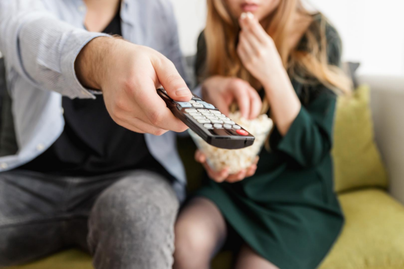 Couple sits on the couch with popcorn and a remote