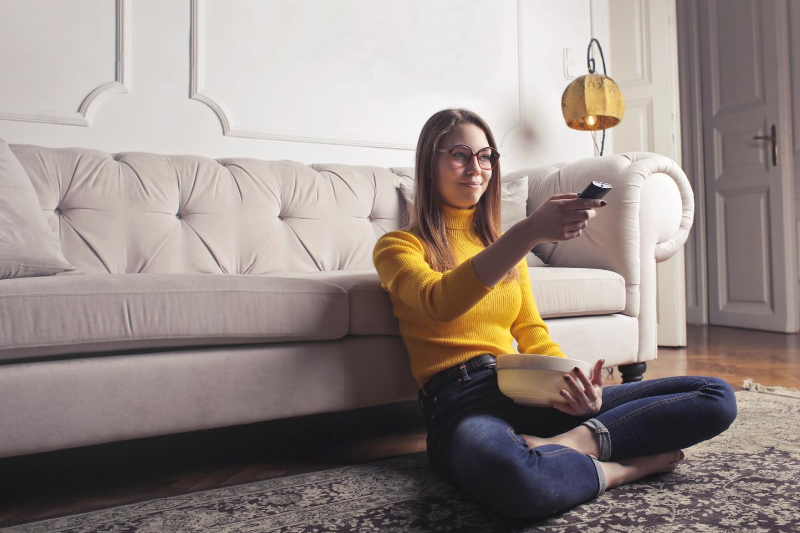 A woman sits cross-legged on the floor with a remote in front of the couch
