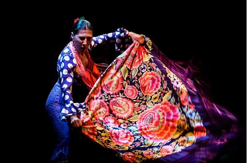 A woman in a polka dot dress fans out a flowered shawl