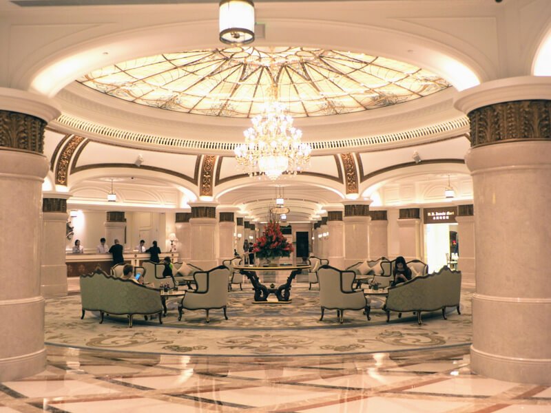 ornate lobby with marble floors, an enormous blue carpet, a glass ceiling and a crystal chandelier
