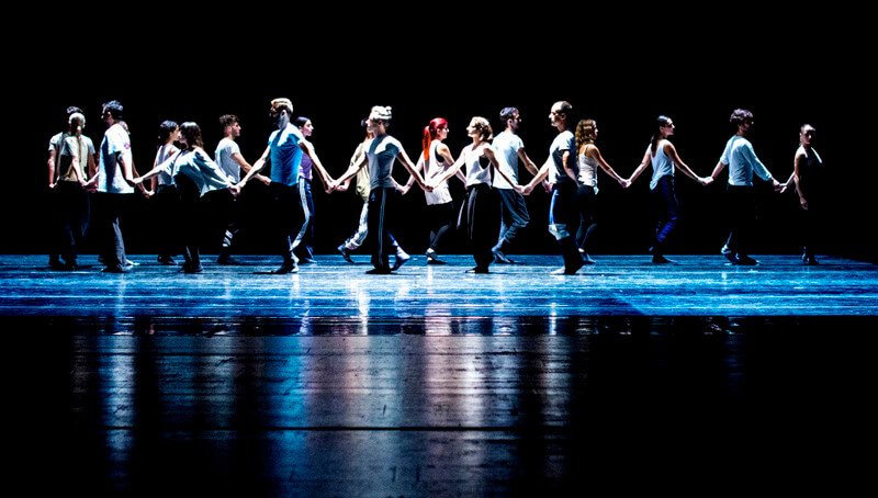 Dancers hold hands and perform in piece referencing traditional Greek dances