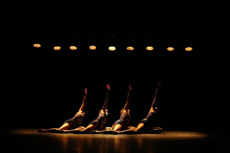 Four seated women reach up towards the yellow light