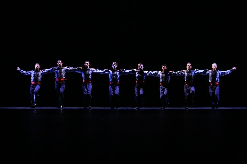 Men link arms and dance in a line