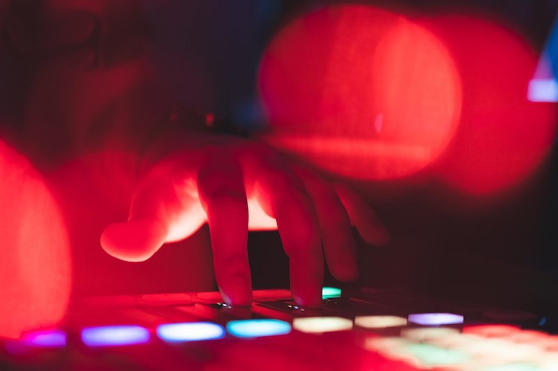 A hand touches DJ equipment with multi-colored lights