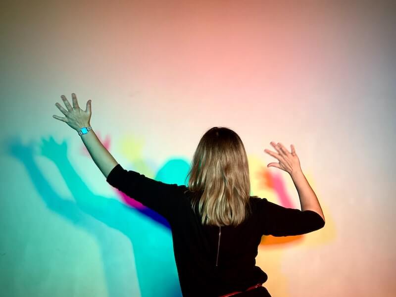 A woman stretches her arms in colored lights