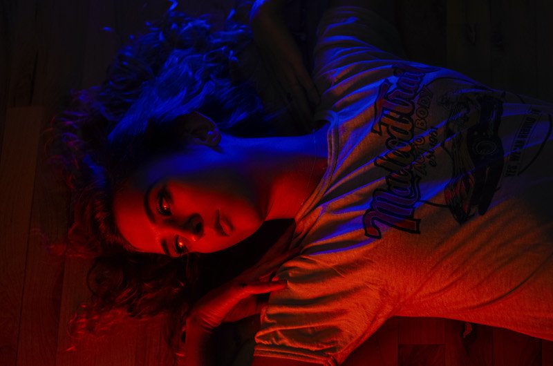 A woman in a t-shirt lies on the floor, illuminated by red and blue lights