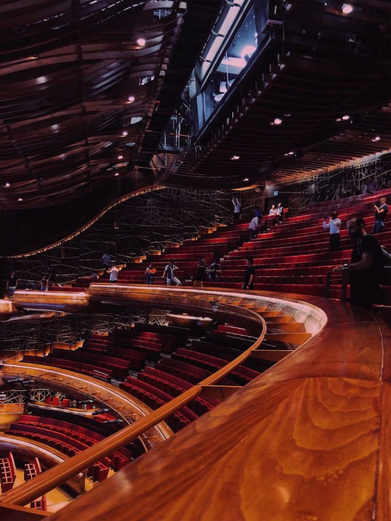 A railing cures to the left in a theatre full of plush red seats
