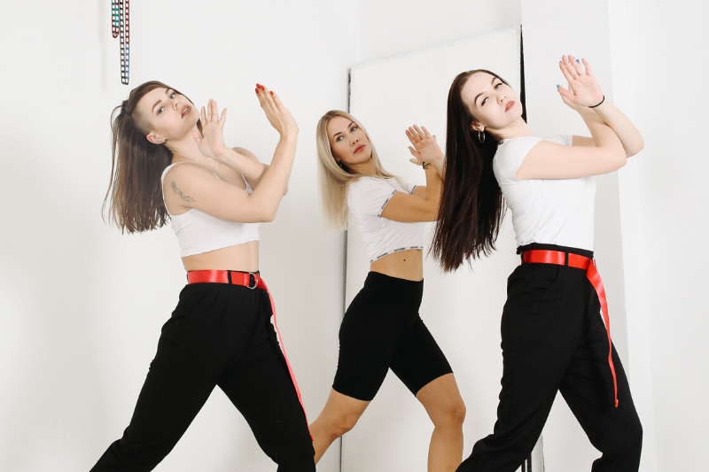 Three girls in white shirts and black trousers dancing in white room